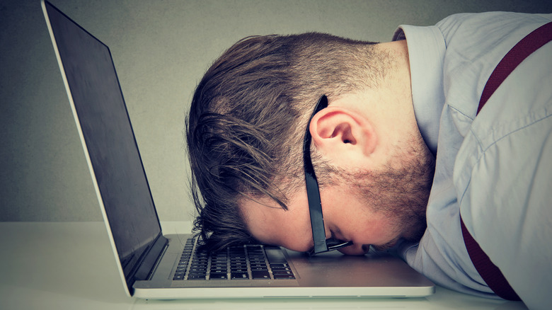 Laptop user resting head on device in frustration