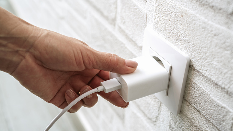 Close-up of a hand touching a phone charger plugged into a wall