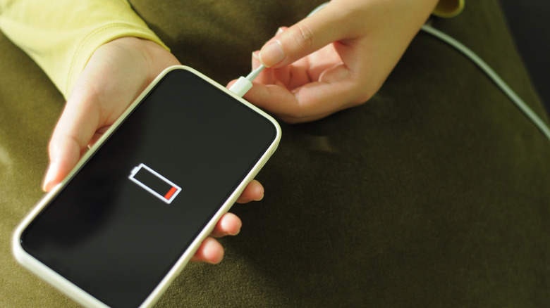 A hand pluggig a phone with a very low battery symbol on the screen into a charger