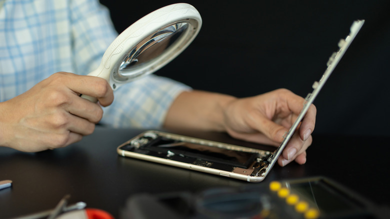 A repair technician examining the inside of a faulty smartphone