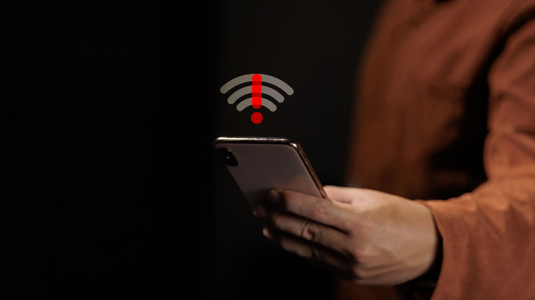 A person holding a device with a Wi-Fi symbol over it with an exclamation mark