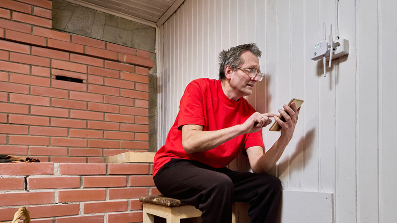 A man searching for a Wi-Fi signal on his phone near the router