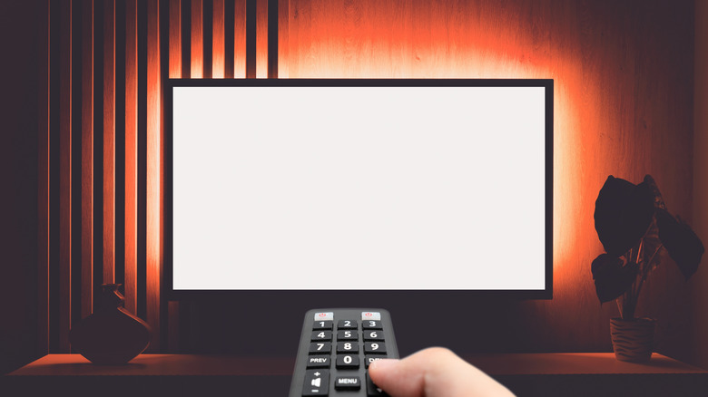 A blank TV in the background a person holding the remote infront