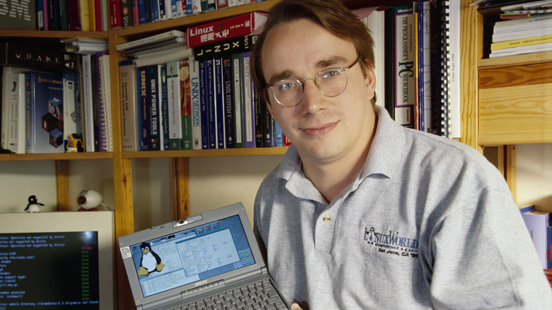 Linus Torvalds, the creator of Linux, posing with Linux open on a small device with books in the background.