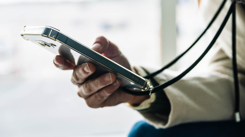 Person holding a smartphone attached to a black lanyard.