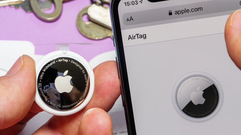 Close-up of an Apple AirTag held beside an iPhone showing the AirTag page.