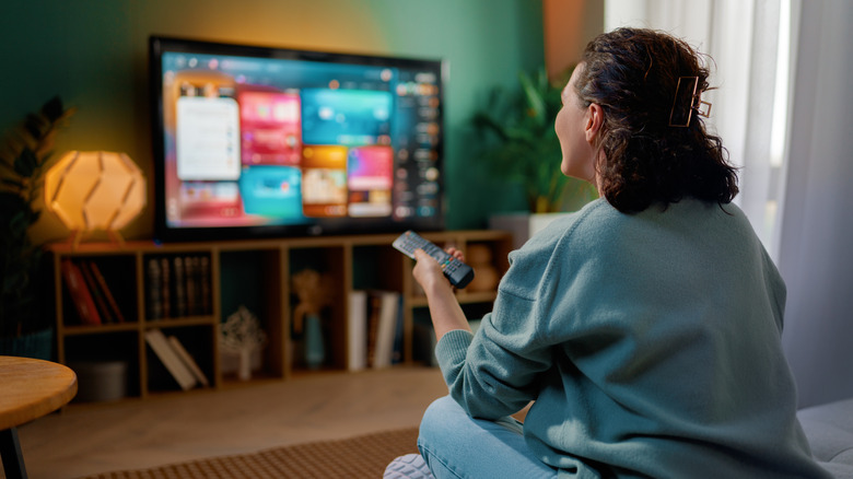 Person using a remote to browse a smart TV menu in a cozy living room.