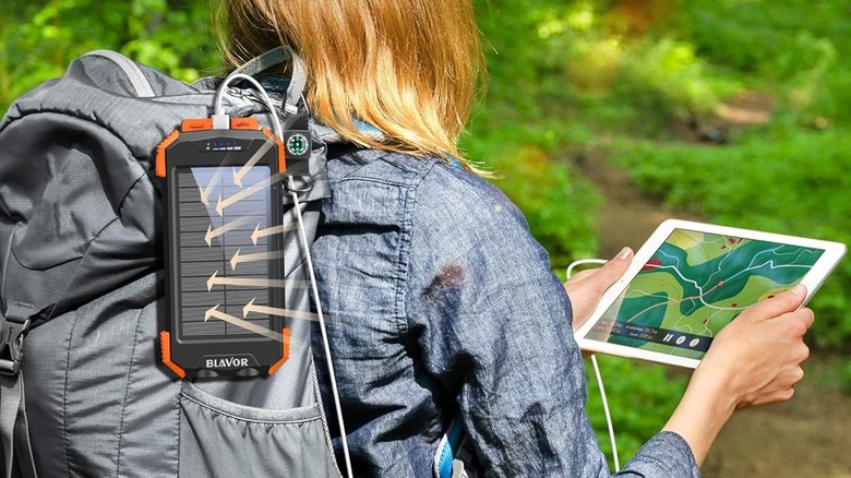 Close up of a woman walking through the woods navigating on a tablet that's plugged into a solar powered charger