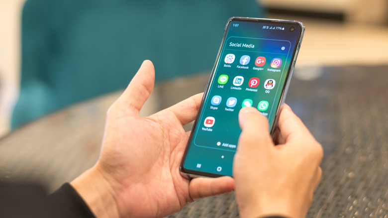 A person holding a phone while navigating to social media apps
