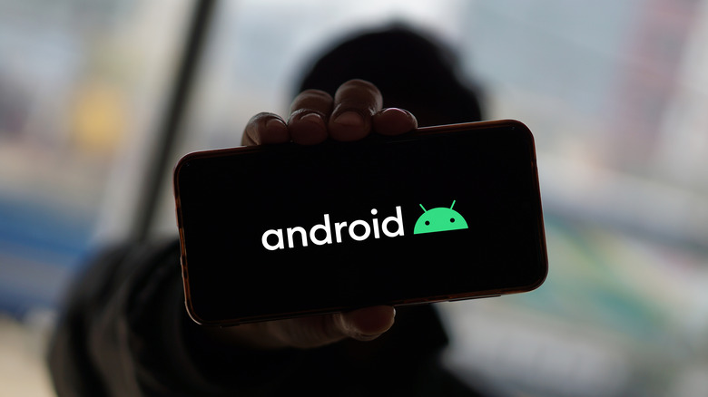 A person holding out a phone with the Android logo on its screen