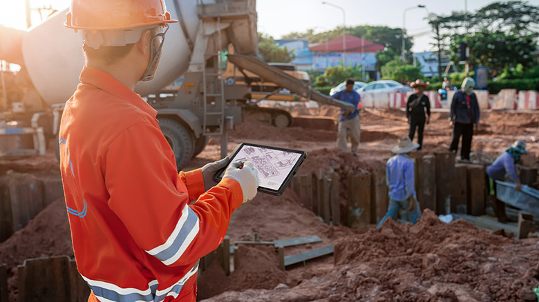 A man on a construction site looking at plans on a Lenovo ThinkTab X11 tablet.