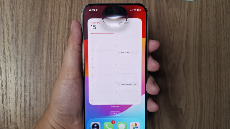 Hand holding iPhone showing Calendar widget with Siri activated