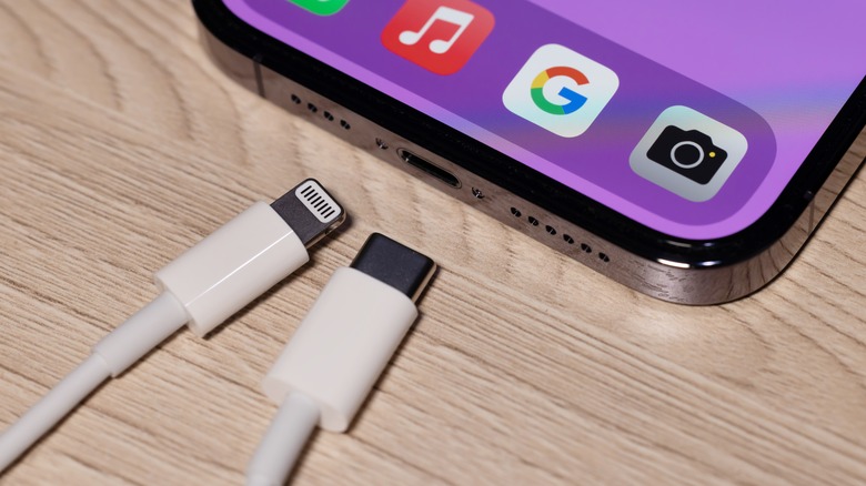 A Lightning cable placed next to a USB-C cable, both of which are near the charge port of an iPhone.