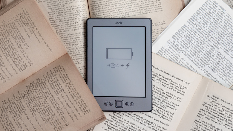 A low-battery Kindle amongst a pile of open books