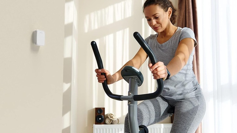 A person exercising in a room with a thermostat on a nearby wall