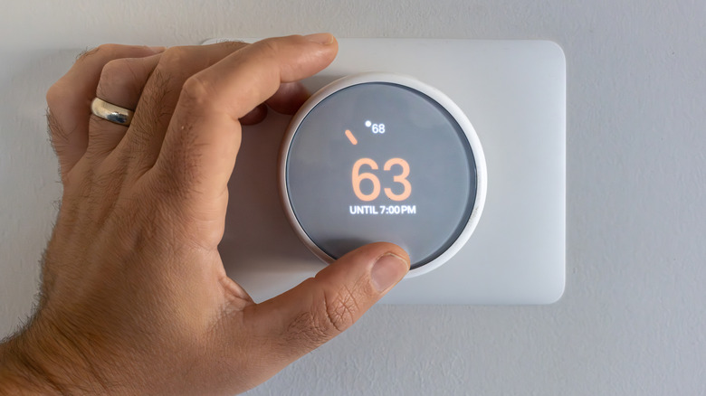 A hand adjusting a smart thermostat on a white wall