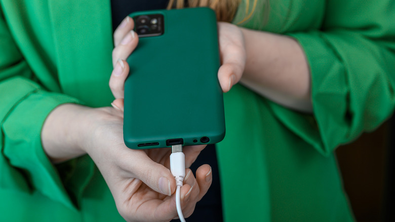 A woman in green plugging a phone into a USB-C cable.