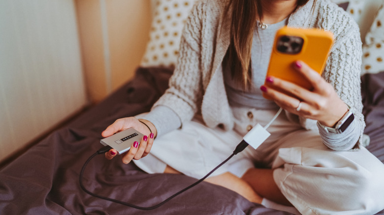 A woman with a phone connected to a portable hard drive.