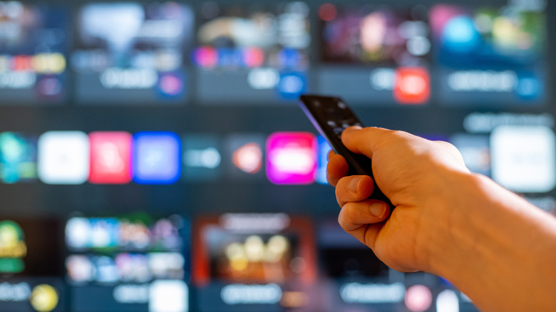 Hand holding a remote pointed toward a blurred smart Tv screen