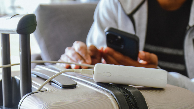 Man using power bank to charge phone resting on luggage.