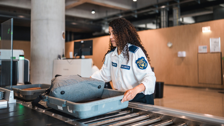 TSA security agent checking bags on conveyor.