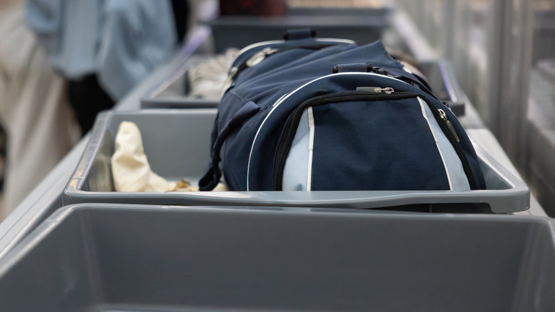 A backpack on a grey tray about to go into an X-Ray scanner
