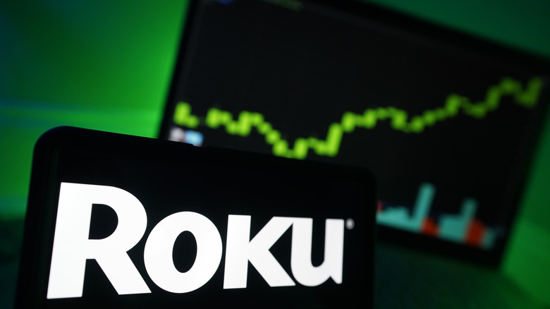 The Roku logo on a phone in front of a stock chart.