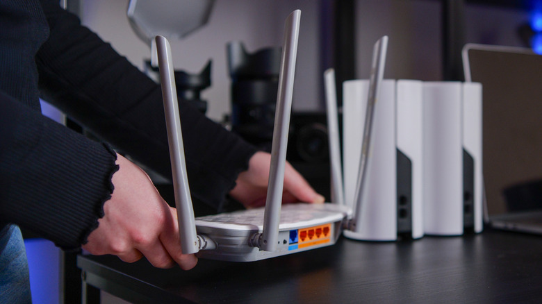 A person handling a Wi-Fi router on a table with other mesh system nodes