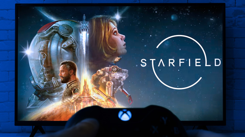 Person holding an Xbox controller with TV in the background.