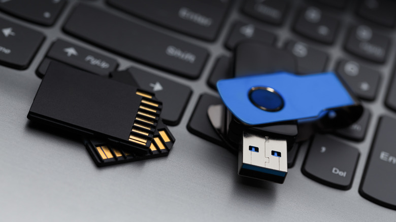 A close up of SD cards stacked next to a USB flash drive on a keyboard.