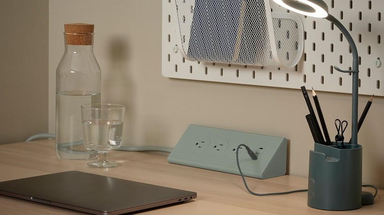 A Skotat Extension Cord placed on a desk surrounded by a laptop, desk lamp, and a water bottle