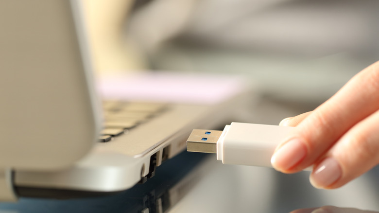 A person inserting a USB gadget into a laptop's USB port.