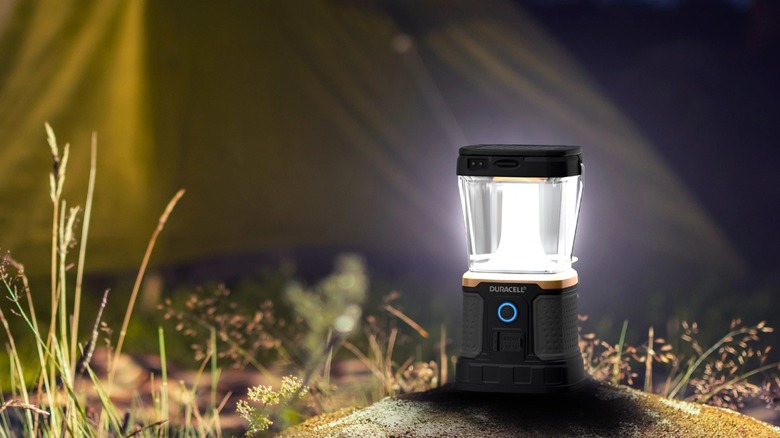 The Duracell 3000 L Tri Power Rechargeable Lantern turned on, placed on the ground outside of a tent.