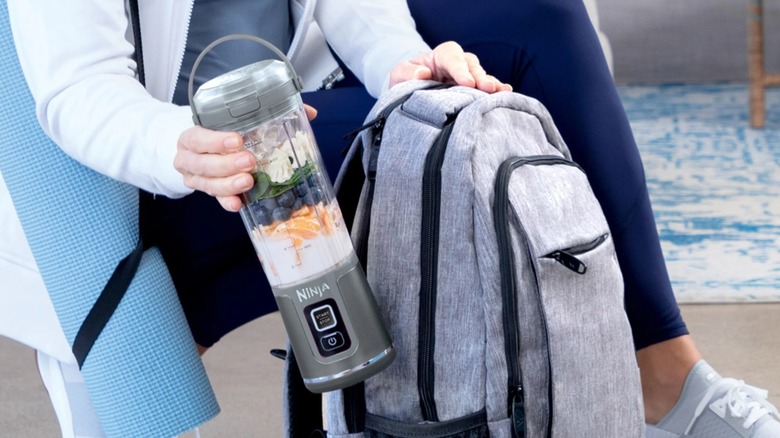 A person placing the Ninja Blast 18 oz. Portable Blender in a backpack's outer pocket.