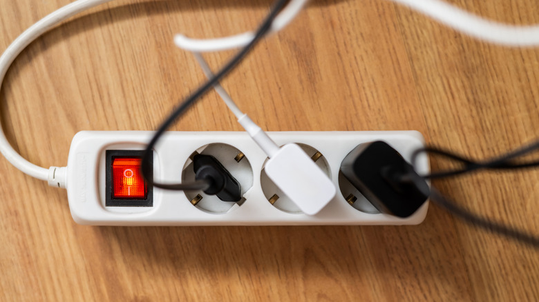 A white power strip lays on a woodgrain surface with three cords plugged into it