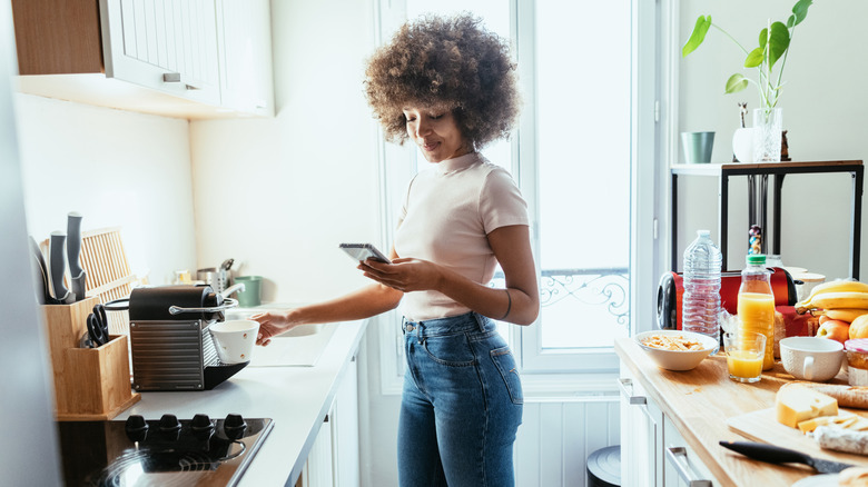 A woman making cup of coffee while using her phone.