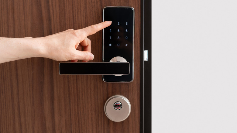 A person pointing to a smart lock keypad on the outside of a door.
