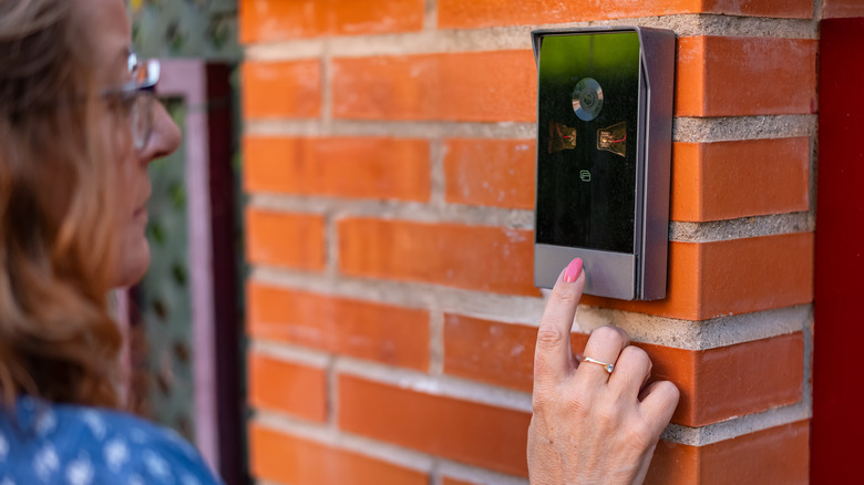Close-up of a person ringing a video doorbell mouted on the exterior of a house