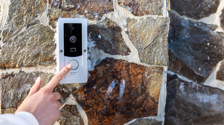 Close-up of a person pressing a video doorbell button mounted on a stone wall