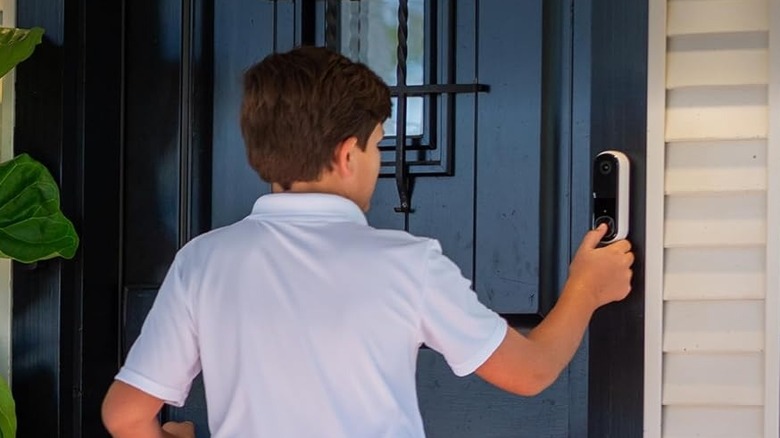 A young man ringing an Arlo Video Doorbell HD (2nd Gen) mounted outside a front door.