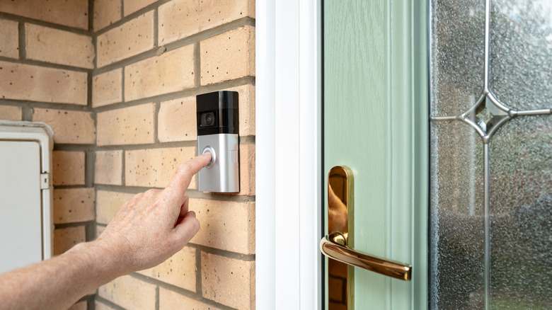 A person ringing a Ring video doorbell mounted to exterior brick.