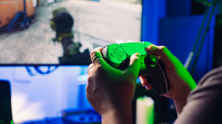 A person holding a PlayStation controller and playing a game next to a screen