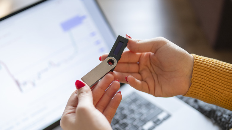 A person holding a USB flash drive in front of a laptop