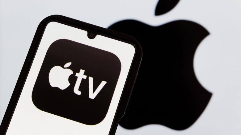 A smartphone displaying the Apple TV logo as it sits in front of a silver backdrop also displaying an Apple logo