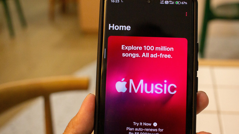 An individual holds a smartphone in their right hand as the device displays an advertisement for Apple Music