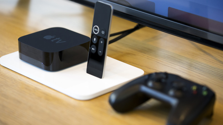 The Apple TV 4K with a remote control and a joystick on a wooden table