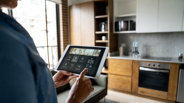 Person in blue shirt monitoring smart home devices via tablet in kitchen