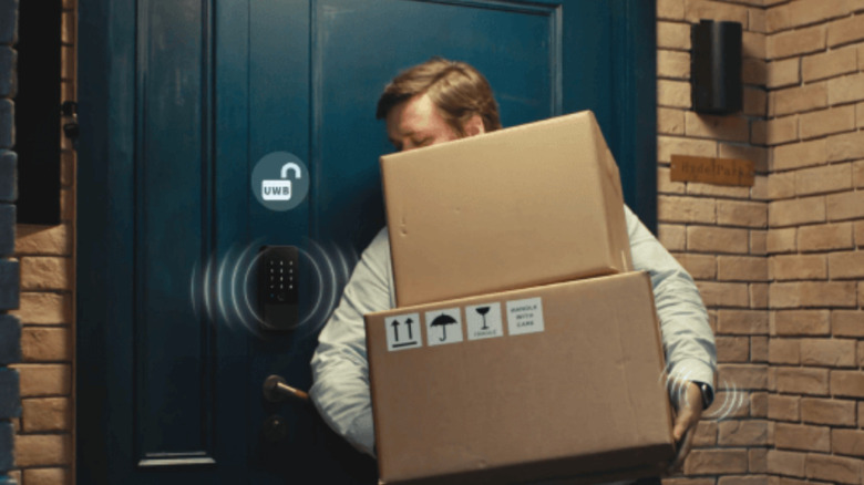 Man carrying two boxes unlocking door with smartwatch