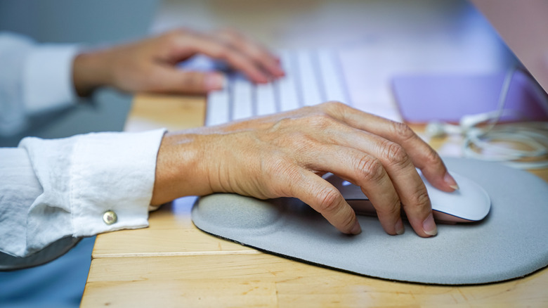 Hands atop a keyboard and mouse at a desk.