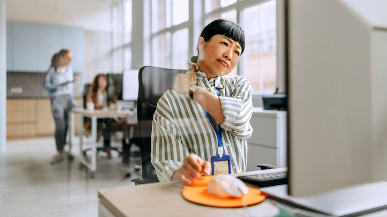A woman sitting at her desk holding her neck in pain.